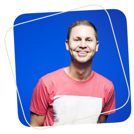 A music producer in a red shirt smiling in front of a blue background at Producerboutique.